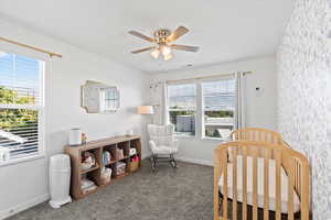 Carpeted bedroom with ceiling fan and a crib