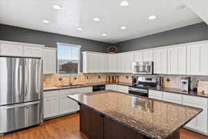 Kitchen with dark stone countertops, white cabinets, appliances with stainless steel finishes, and a kitchen island