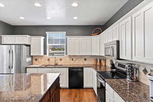 Kitchen featuring white cabinets, appliances with stainless steel finishes, sink, and dark stone counters