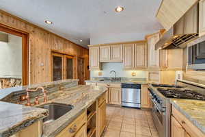 Kitchen with appliances with stainless steel finishes, light brown cabinets, wood walls, and sink