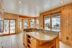 Kitchen with sink, wooden walls, a kitchen island with sink, and a notable chandelier