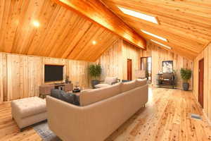 Living room with wood walls, vaulted ceiling with skylight, light hardwood / wood-style flooring, and wooden ceiling