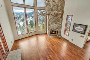 Unfurnished living room featuring a stone fireplace, wood-type flooring, and a towering ceiling