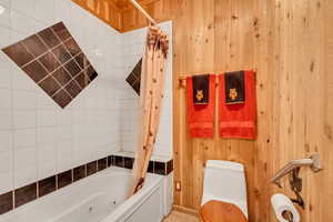 Bathroom with wooden walls, shower / tub combo with curtain, and toilet