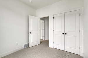 Unfurnished bedroom featuring a closet, visible vents, light colored carpet, and baseboards