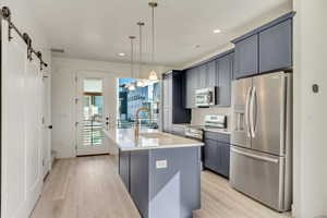 Kitchen with a center island with sink, a barn door, light wood-type flooring, pendant lighting, and stainless steel appliances