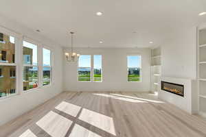 Unfurnished living room with a chandelier, built in features, and light wood-type flooring