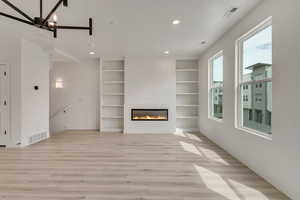 Unfurnished living room featuring a glass covered fireplace, visible vents, light wood-style floors, and recessed lighting