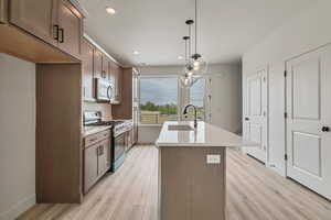 Kitchen featuring appliances with stainless steel finishes, an island with sink, light wood-style flooring, and a sink