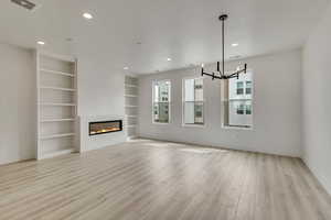 Unfurnished living room featuring visible vents, light wood-style floors, baseboards, a notable chandelier, and built in shelves