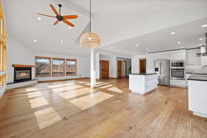 Kitchen with high vaulted ceiling, stainless steel appliances, white cabinetry, light hardwood / wood-style flooring, and decorative light fixtures