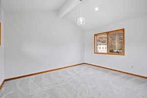 Empty room with lofted ceiling with beams and carpet flooring