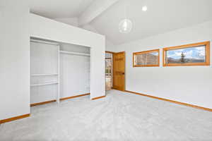 Unfurnished bedroom with a closet, vaulted ceiling with beams, and light carpet