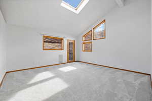 Spare room with a skylight, high vaulted ceiling, and light carpet