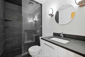 Bathroom with tiled shower, vanity, and toilet