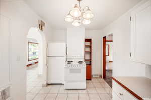 Kitchen featuring white appliances, white cabinetry, pendant lighting, light tile patterned floors, and an inviting chandelier