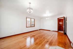 Empty room with a notable chandelier and light wood-type flooring