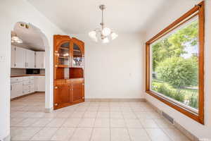 Unfurnished dining area featuring light tile patterned flooring and an inviting chandelier