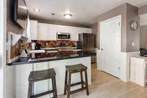 Kitchen featuring light hardwood / wood-style floors, sink, kitchen peninsula, appliances with stainless steel finishes, and white cabinetry