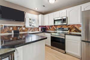 Kitchen with light wood-type flooring, sink, kitchen peninsula, white cabinets, and appliances with stainless steel finishes