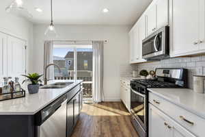 Kitchen with appliances with stainless steel finishes, sink, dark hardwood / wood-style flooring, white cabinetry, and decorative light fixtures