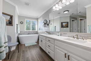 Bathroom featuring solid surface / wood-style flooring, a tub to relax in, crown molding, and vanity