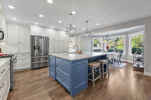 Kitchen featuring laminate/wood-style floors, decorative light fixtures, an island with sink, appliances with stainless steel finishes, and white cabinetry