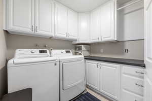 Clothes washing area with washer and clothes dryer, light tile patterned floors, and cabinets