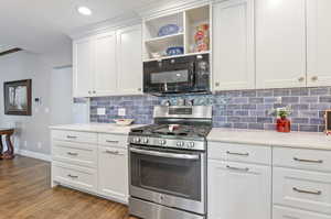 Kitchen with white cabinetry, laminate/wood-style floors, gas range, and backsplash