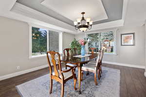 Dining space with ornamental molding, laminate/wood-style floors, an inviting chandelier, and a raised ceiling