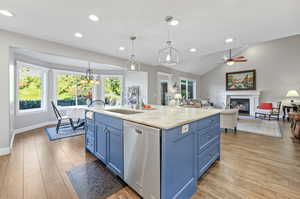 Kitchen featuring laminate/wood-style floors, hanging light fixtures, a center island with sink, blue cabinets, and dishwasher