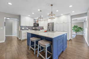 Kitchen with laminate/wood-style floors, white cabinets, appliances with stainless steel finishes, and hanging light fixtures