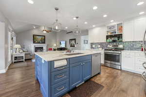 Kitchen featuring sink, laminate/wood-style floors, white cabinetry, blue cabinetry, and appliances with stainless steel finishes