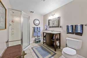 Bathroom featuring vanity, toilet, a textured ceiling, walk in shower, and tile patterned flooring