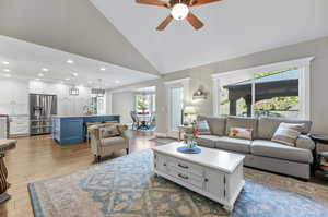 Living room with laminate/wood-style floors, ceiling fan with notable chandelier, sink, and high vaulted ceiling