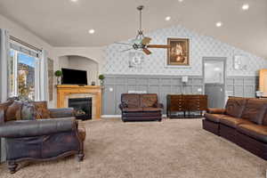 Carpeted living room featuring ceiling fan, lofted ceiling, and a tile fireplace