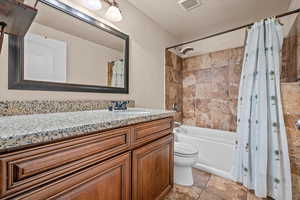 Full bathroom with toilet, a textured ceiling, shower / bath combo with shower curtain, and vanity