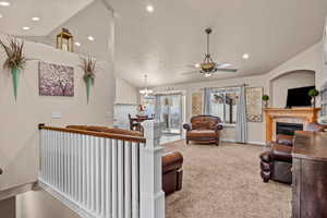 Living room with ceiling fan with notable chandelier, a textured ceiling, a tile fireplace, lofted ceiling, and carpet