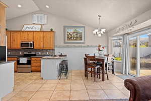 Kitchen with a breakfast bar area, appliances with stainless steel finishes, a chandelier, vaulted ceiling, and pendant lighting