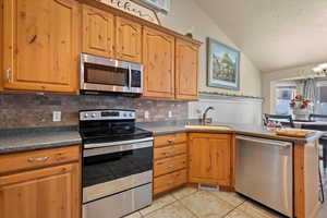 Kitchen with lofted ceiling, decorative backsplash, stainless steel appliances, sink, and a textured ceiling