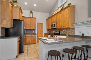 Kitchen with kitchen peninsula, backsplash, sink, a breakfast bar, and appliances with stainless steel finishes