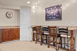 Bar with a textured ceiling, light colored carpet, and light stone counters