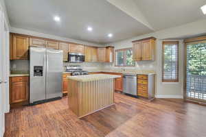 Kitchen featuring lofted ceiling, dark hardwood / wood-style floors, stainless steel appliances, a center island, and light stone counters