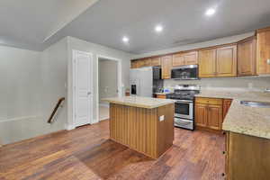 Kitchen with dark hardwood / wood-style flooring, light stone countertops, stainless steel appliances, sink, and a center island