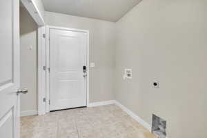 Clothes washing area with hookup for an electric dryer, a textured ceiling, washer hookup, and light tile patterned floors