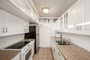 Kitchen featuring light tile patterned flooring, white appliances, white cabinetry, sink, and a textured ceiling