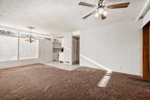 Interior space featuring ceiling fan with notable chandelier, light colored carpet, and a textured ceiling