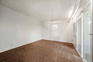 Carpeted spare room featuring a textured ceiling and an AC wall unit