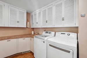 Clothes washing area with cabinets, light hardwood / wood-style flooring, sink, and washing machine and clothes dryer