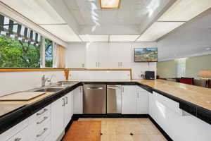 Kitchen featuring sink, stainless steel dishwasher, white cooktop, white cabinets, and light tile patterned floors